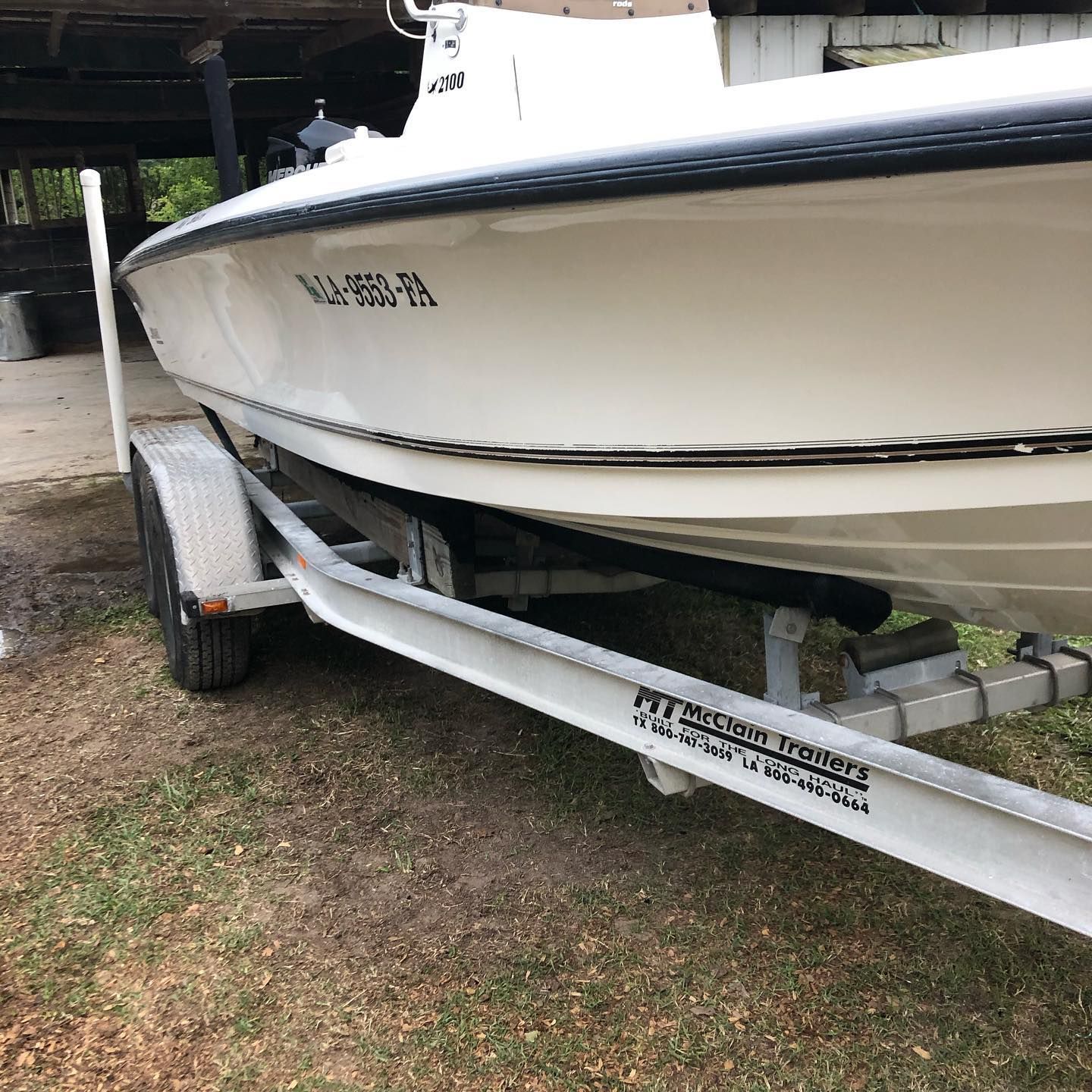 White boat on a trailer in a grassy yard, side view with black trim and dock in background