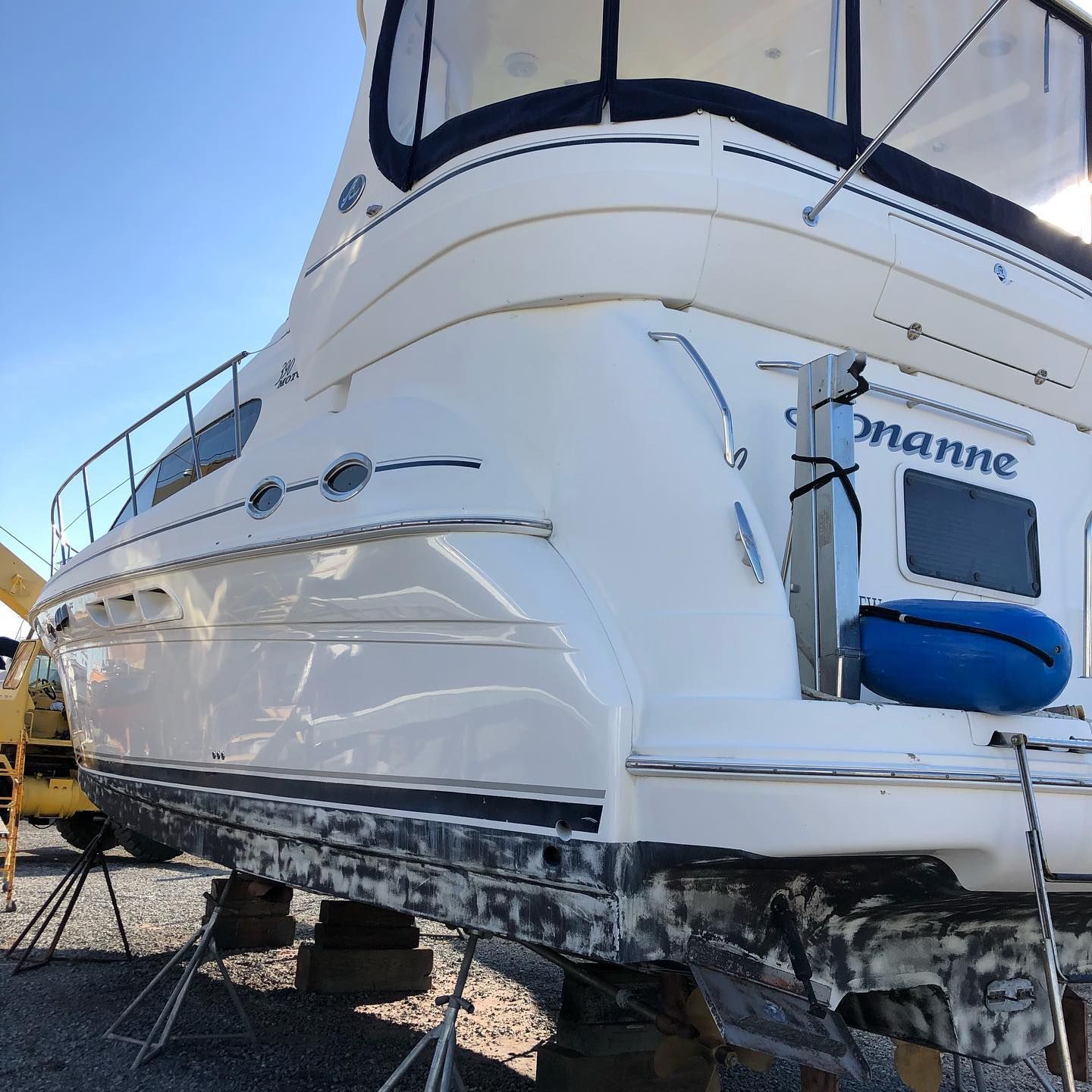 White yacht on land, rear view with blue canvas cover and small blue dinghy at the stern.