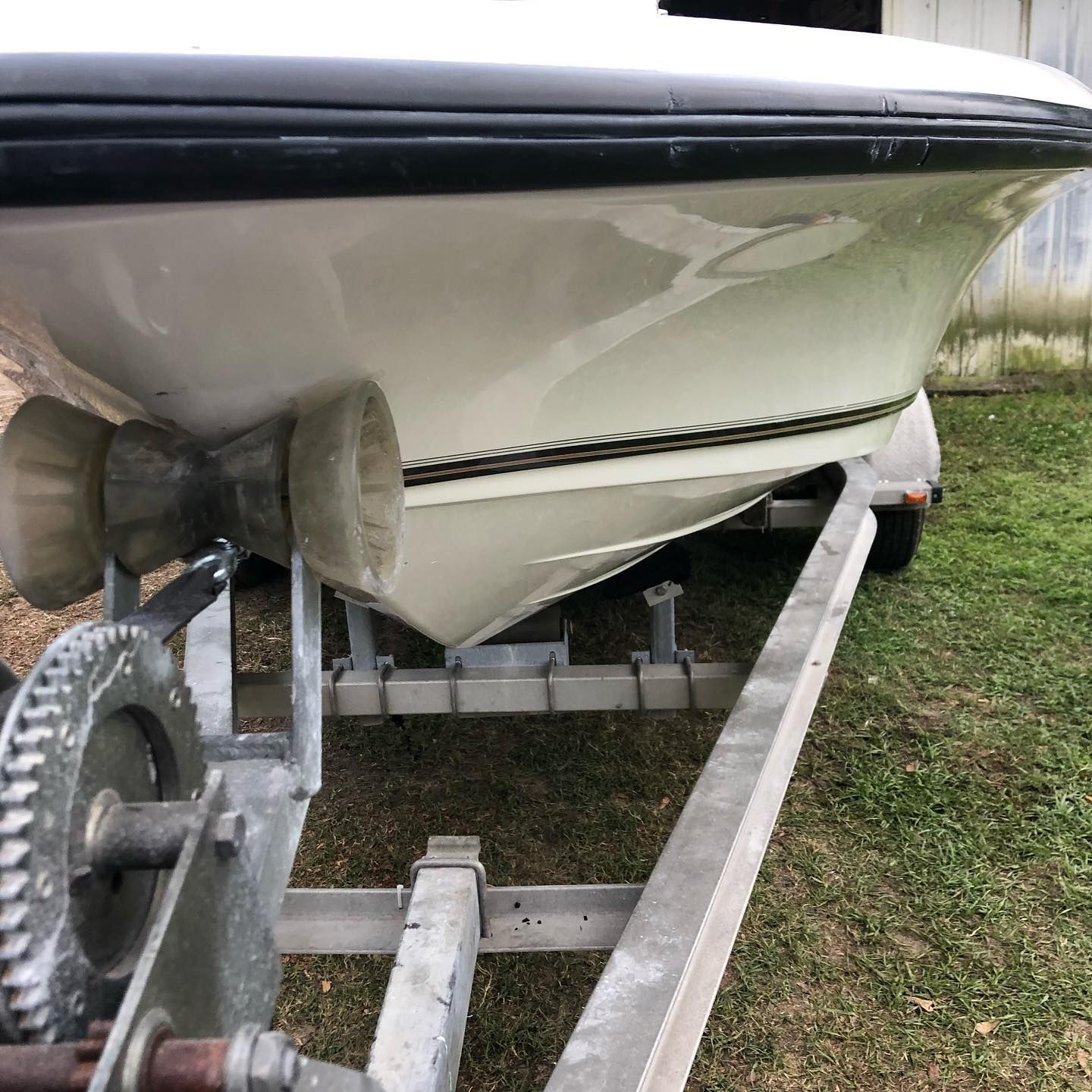 Small motorboat on a trailer, showing the stern and outboard motor near grass.