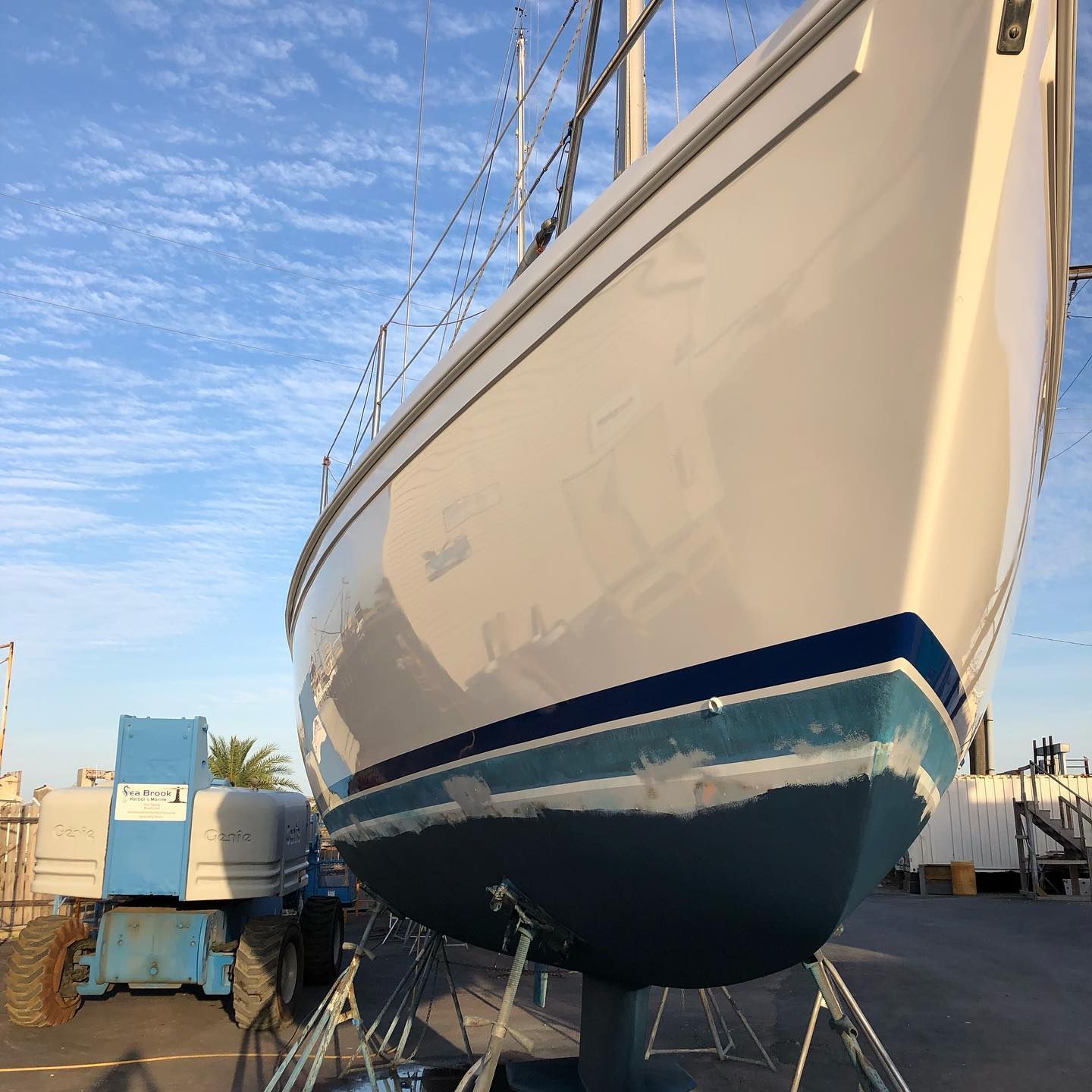 Large white and blue sailboat on land at a boatyard under a clear sky