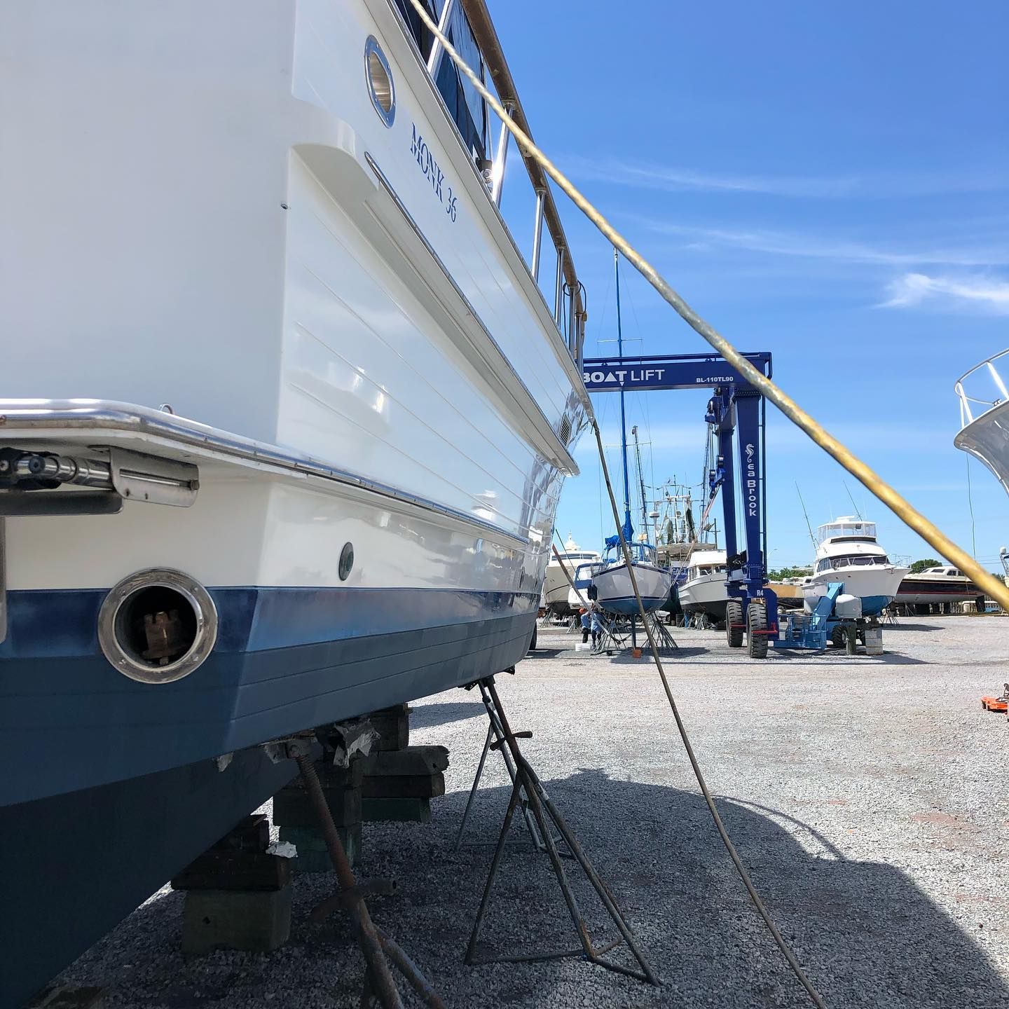 Large white yacht on blocks in a boatyard under a blue sky, with boats and equipment in the background