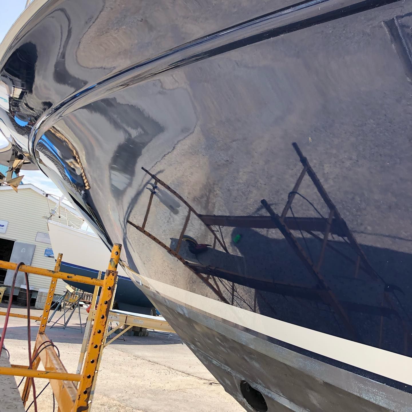 Close-up of a glossy dark-blue boat hull in dry dock, with scaffolding reflected on the surface