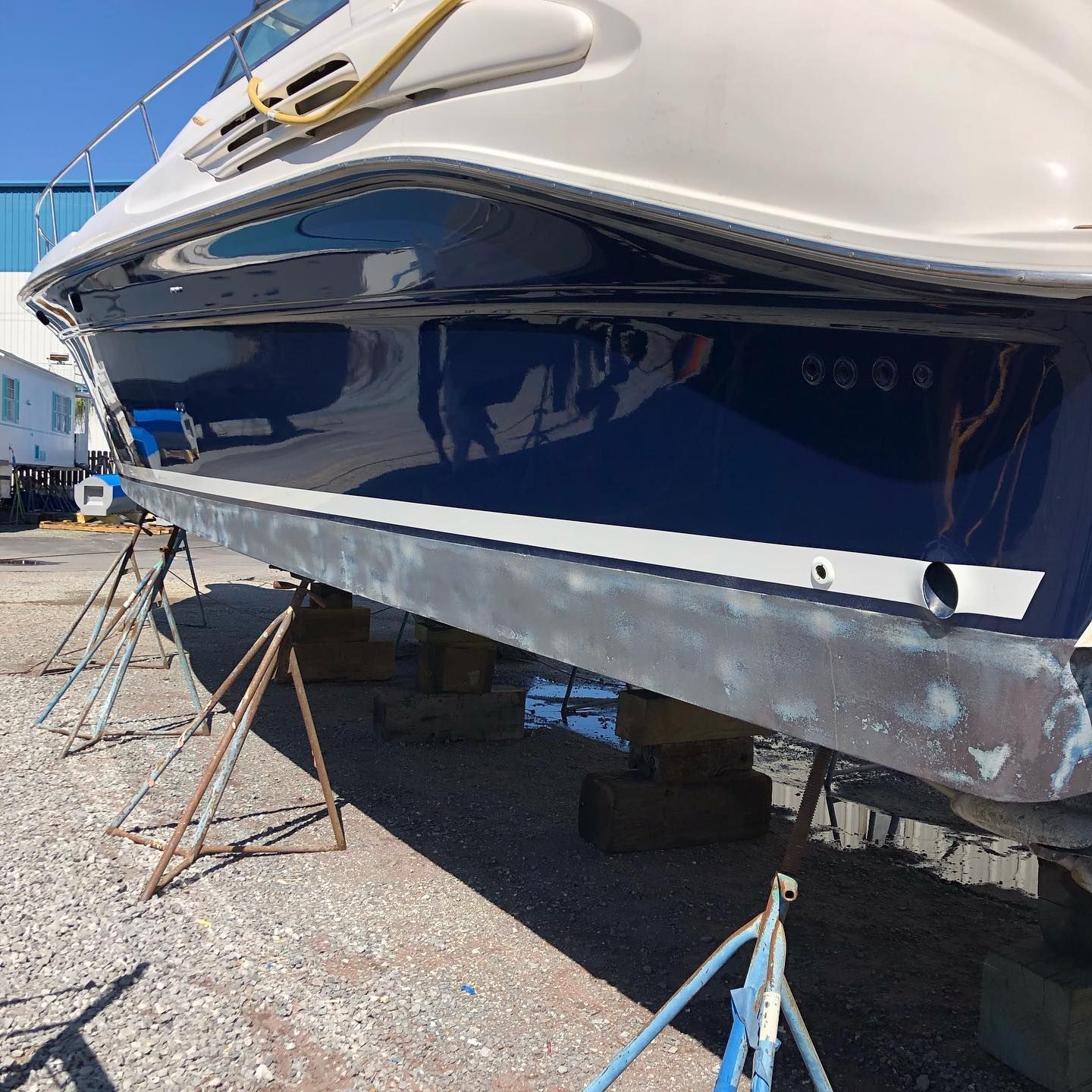 Blue and white boat hull on stands in a boatyard, viewed from below.