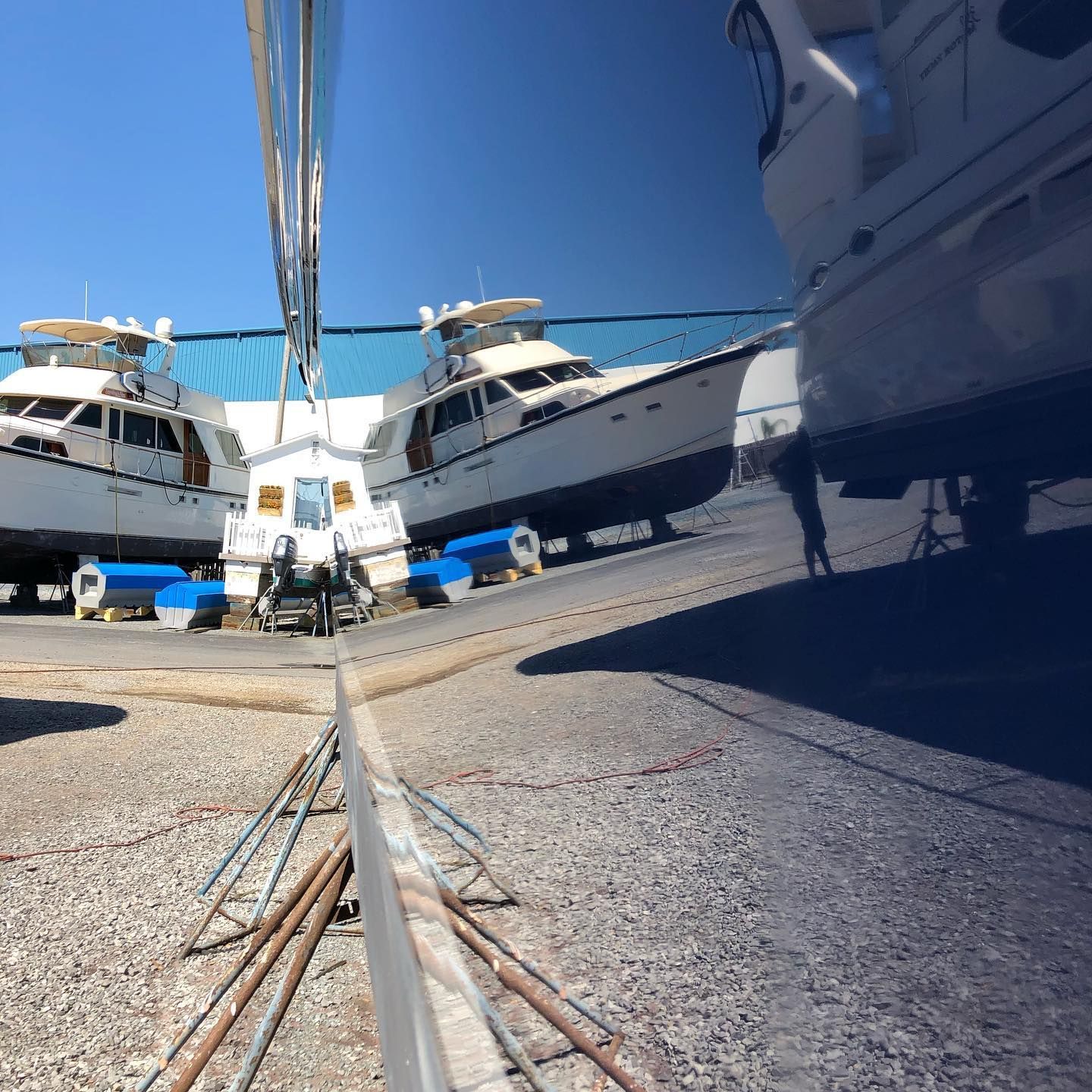 Yachts in a marina, with one boat being hauled up a ramp under a bright blue sky.