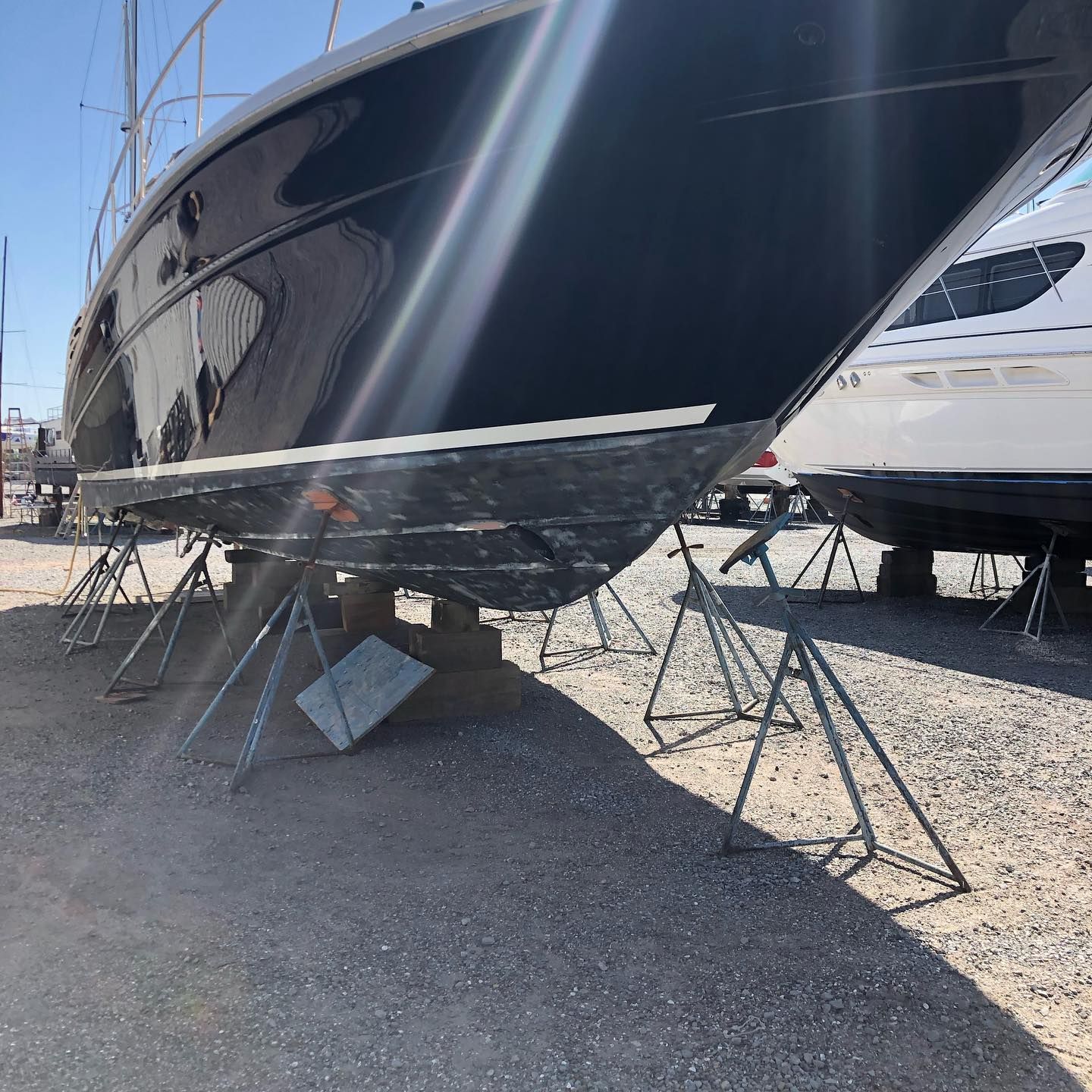 Black sailboat hull on stands in a boatyard, with another white yacht beside it.