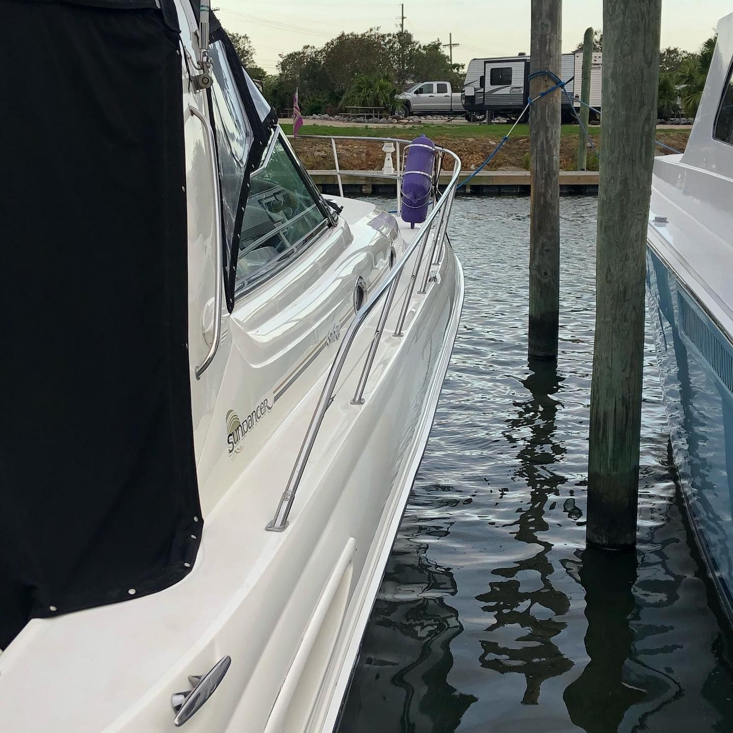 White sailboat tied in a marina beside wooden pilings, with water reflecting the hull.