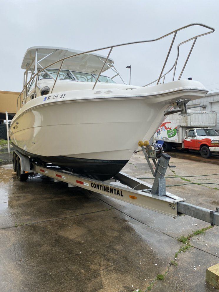 White motorboat on a trailer in a wet parking lot, with a canopy and dock railing visible.
