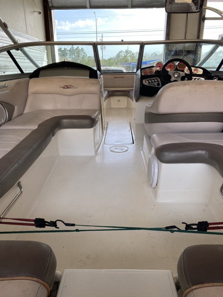 Boat cabin interior with white benches, tan cushions, and steering wheel at the helm.