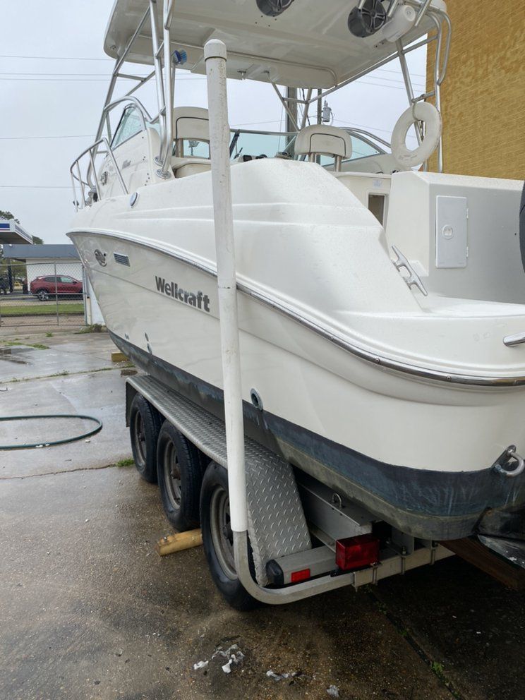 White motorboat on a trailer under a canopy, parked on wet pavement.