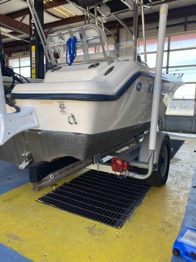 White boat on trailer in indoor storage, with ladder and rack, over a yellow floor mat.