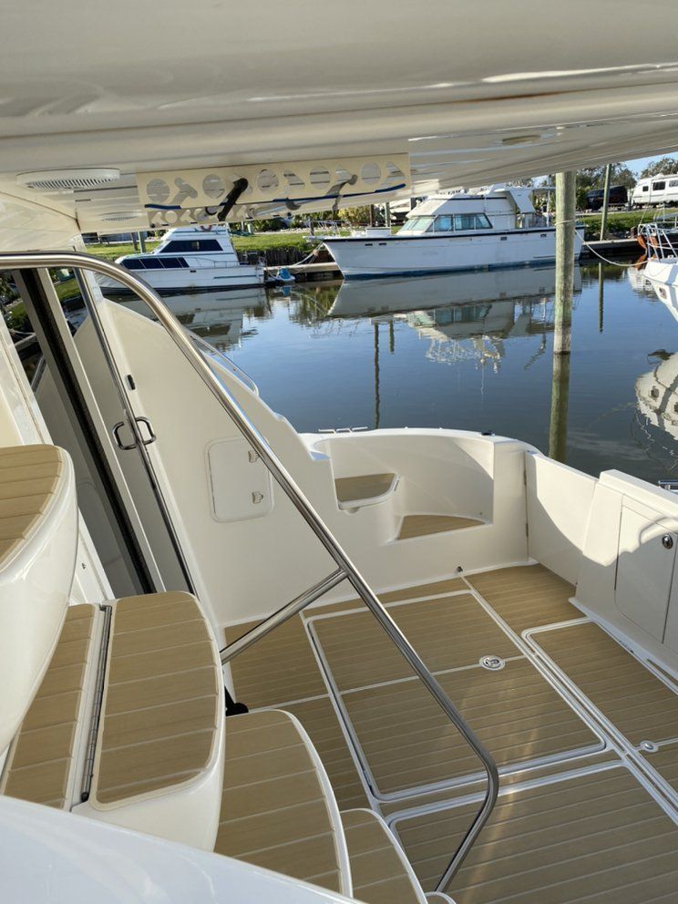 Boat deck with tan flooring and white seating beside calm marina water, under a shaded canopy