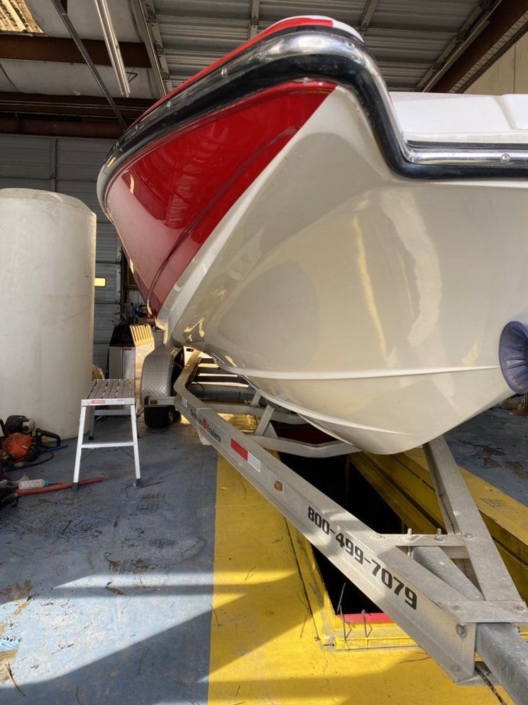 Red and white boat on a trailer inside a workshop, viewed from the stern side.