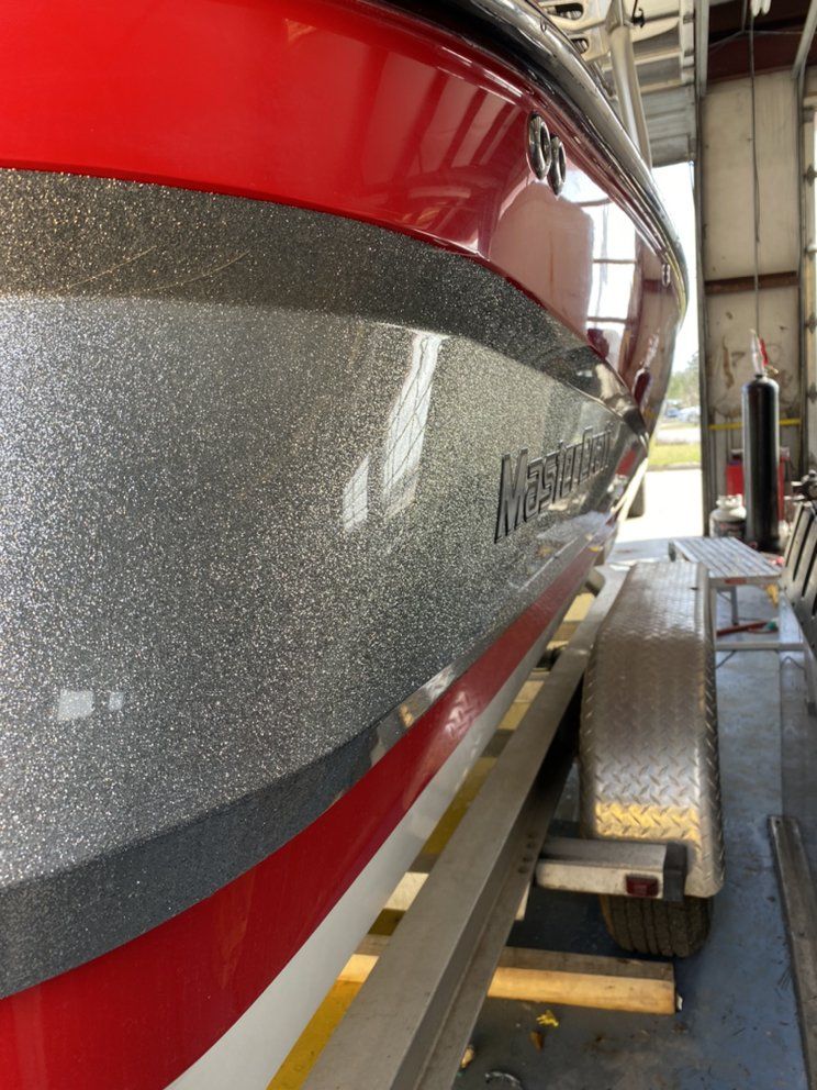Red and silver boat hull in a workshop, with a trailer and ramp beside it