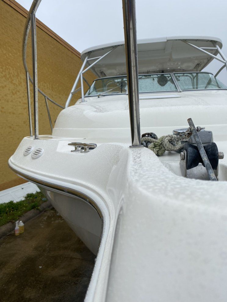 White boat bow docked beside a wall, with mooring lines and an anchor in a narrow marina slip