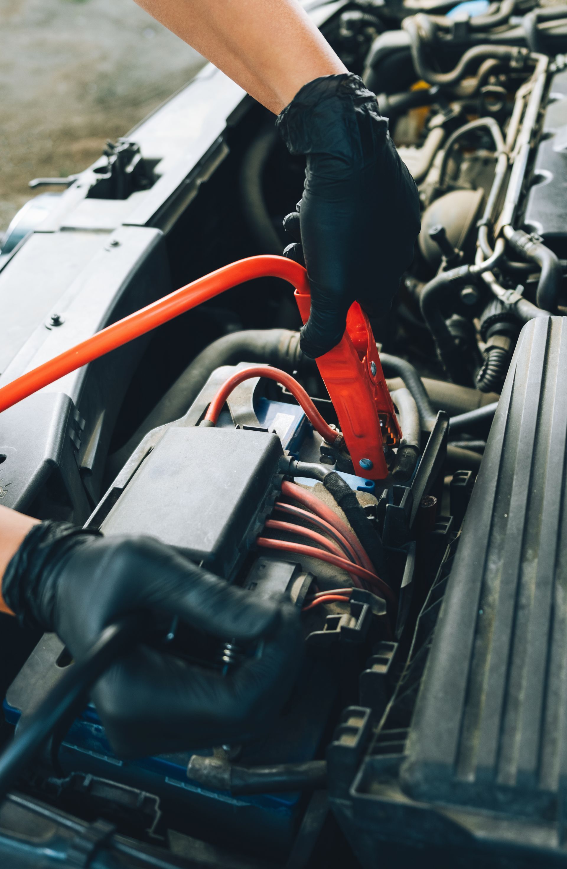 Person connecting jumper cables to a car battery. Person connecting jumper cables to a car battery.