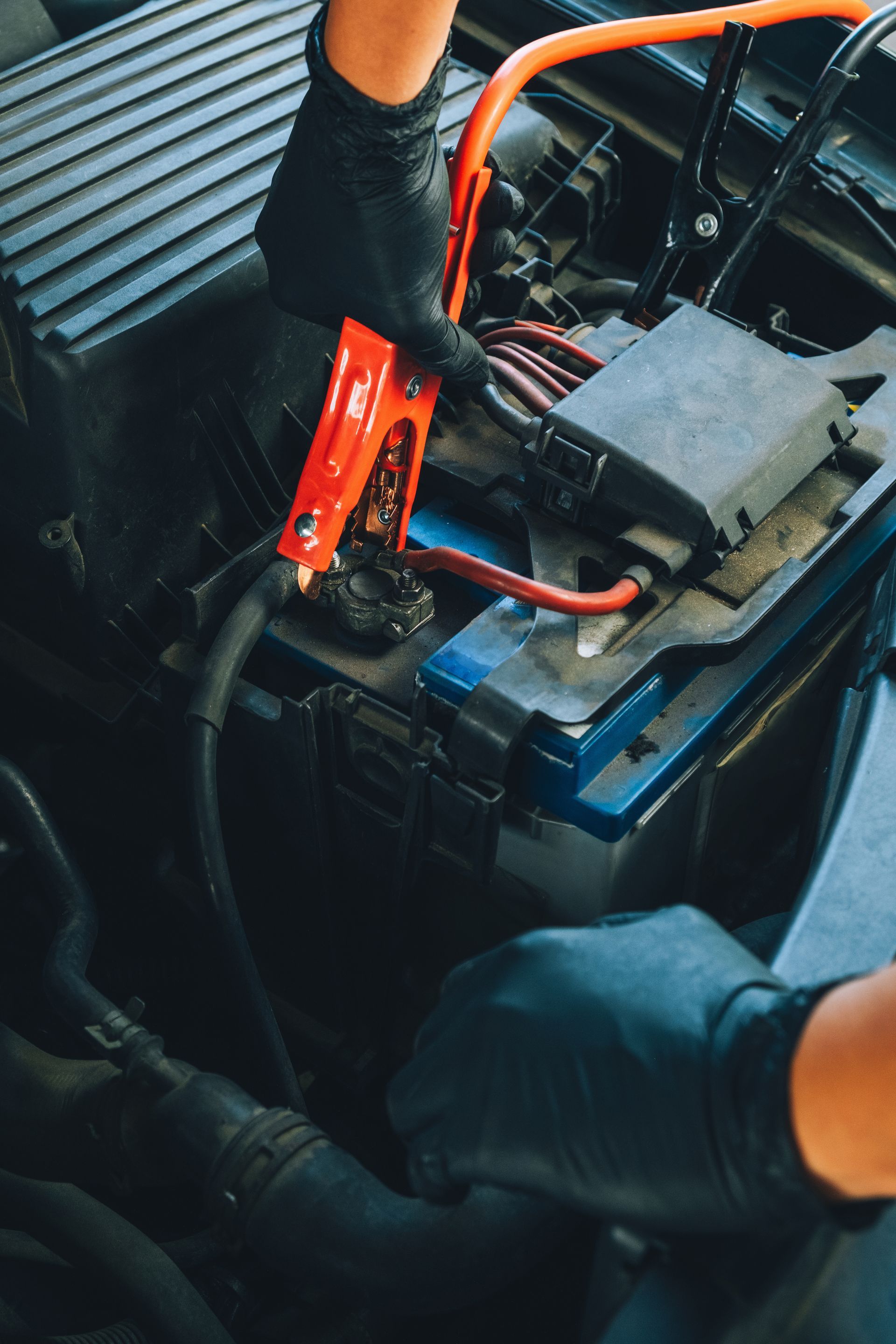 Hands in black gloves connecting jumper cables to a car battery under the hood. Hands in black gloves connecting jumper cables to a car battery under the hood.