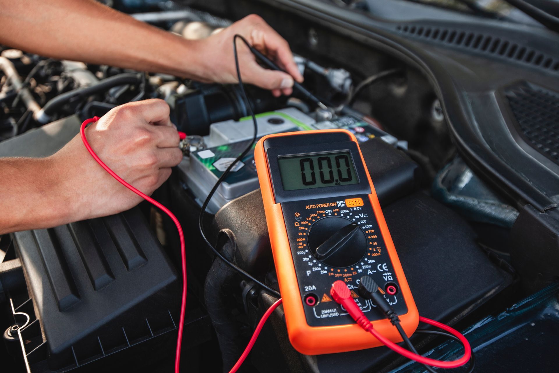 A person tests a car battery with a multimeter under the hood, showing voltage. A person tests a car battery with a multimeter under the hood, showing voltage.