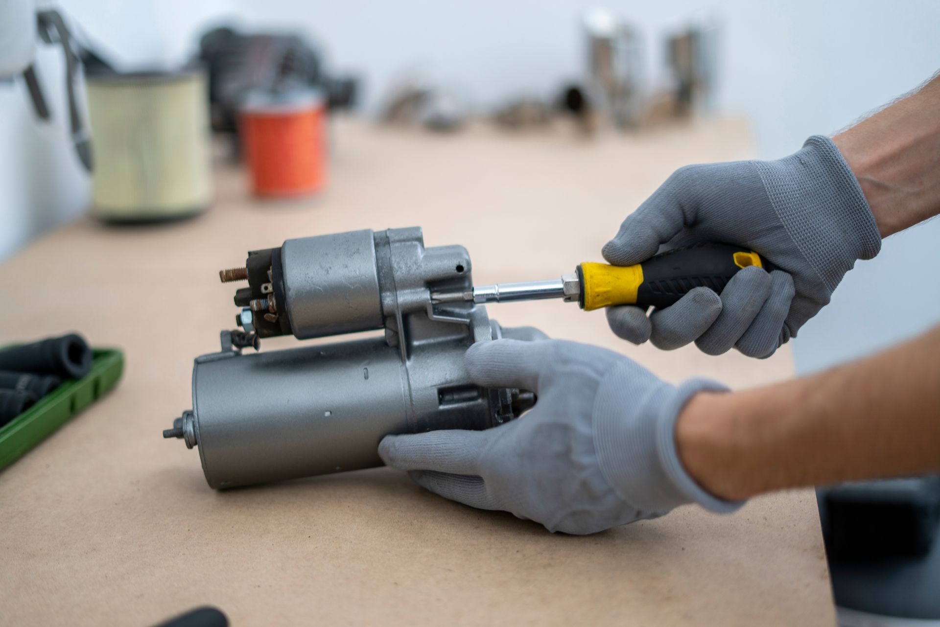 Hands in grey gloves using a screwdriver on a car starter motor in a workshop. Hands in grey gloves using a screwdriver on a car starter motor in a workshop.