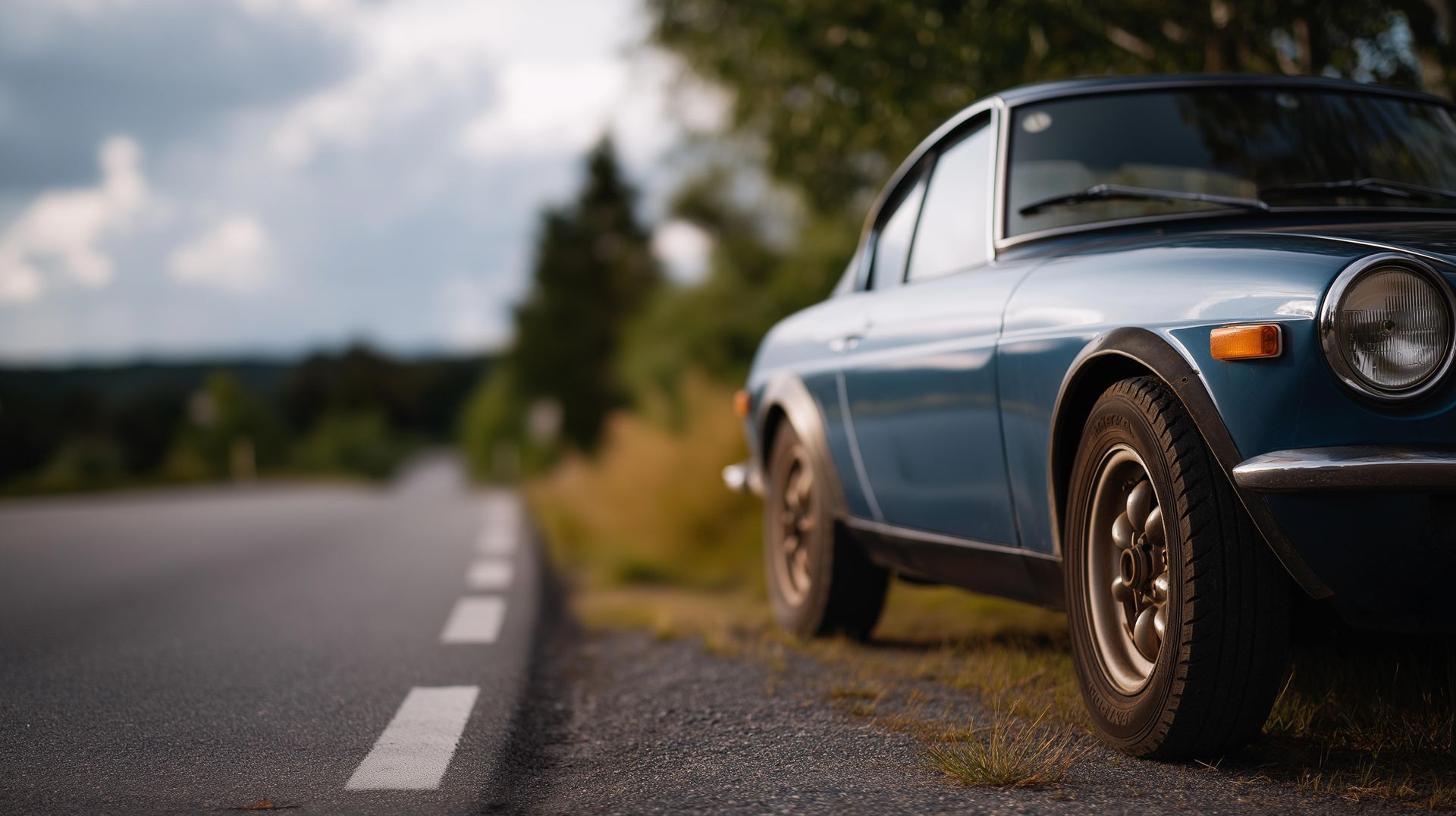 Blue classic car parked on the side of a road, blurred trees and sky in the background. Blue classic car parked on the side of a road, blurred trees and sky in the background.