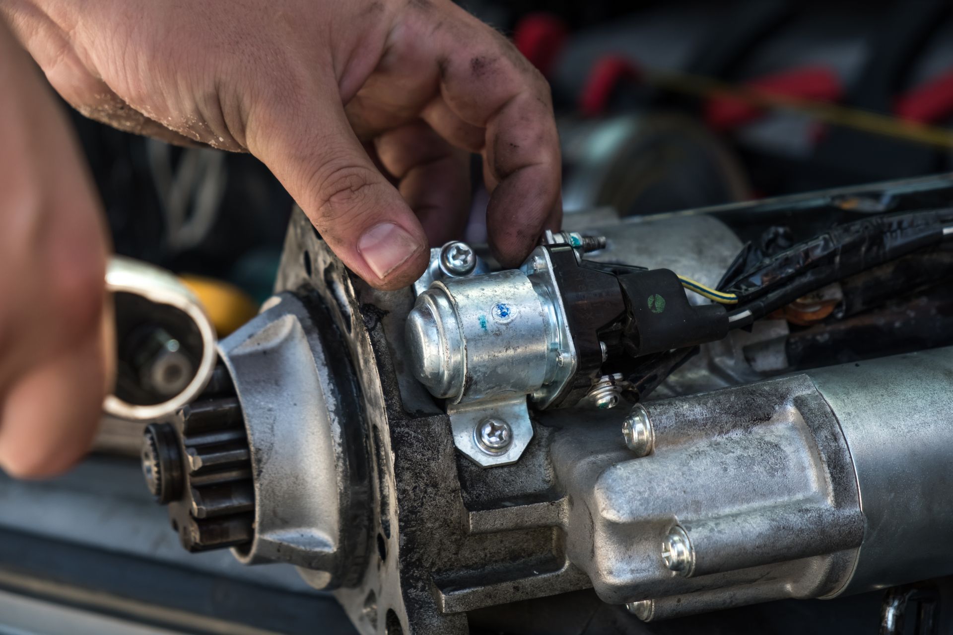 Person's hands working on a car starter motor, fastening a bolt. Person's hands working on a car starter motor, fastening a bolt.