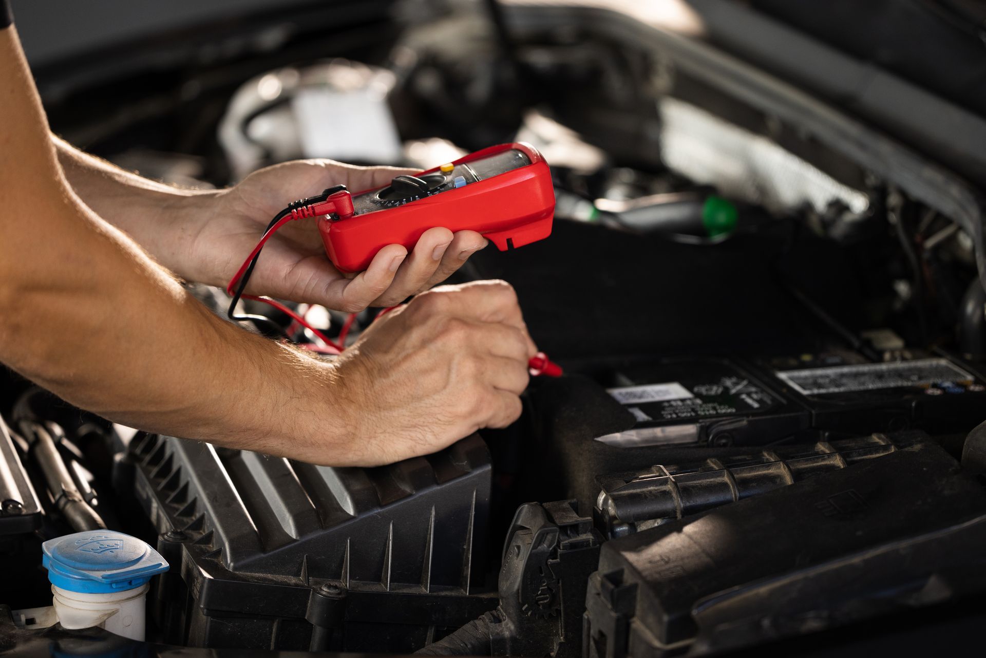Hands holding red multimeter, testing car battery in an open engine bay. Hands holding red multimeter, testing car battery in an open engine bay.