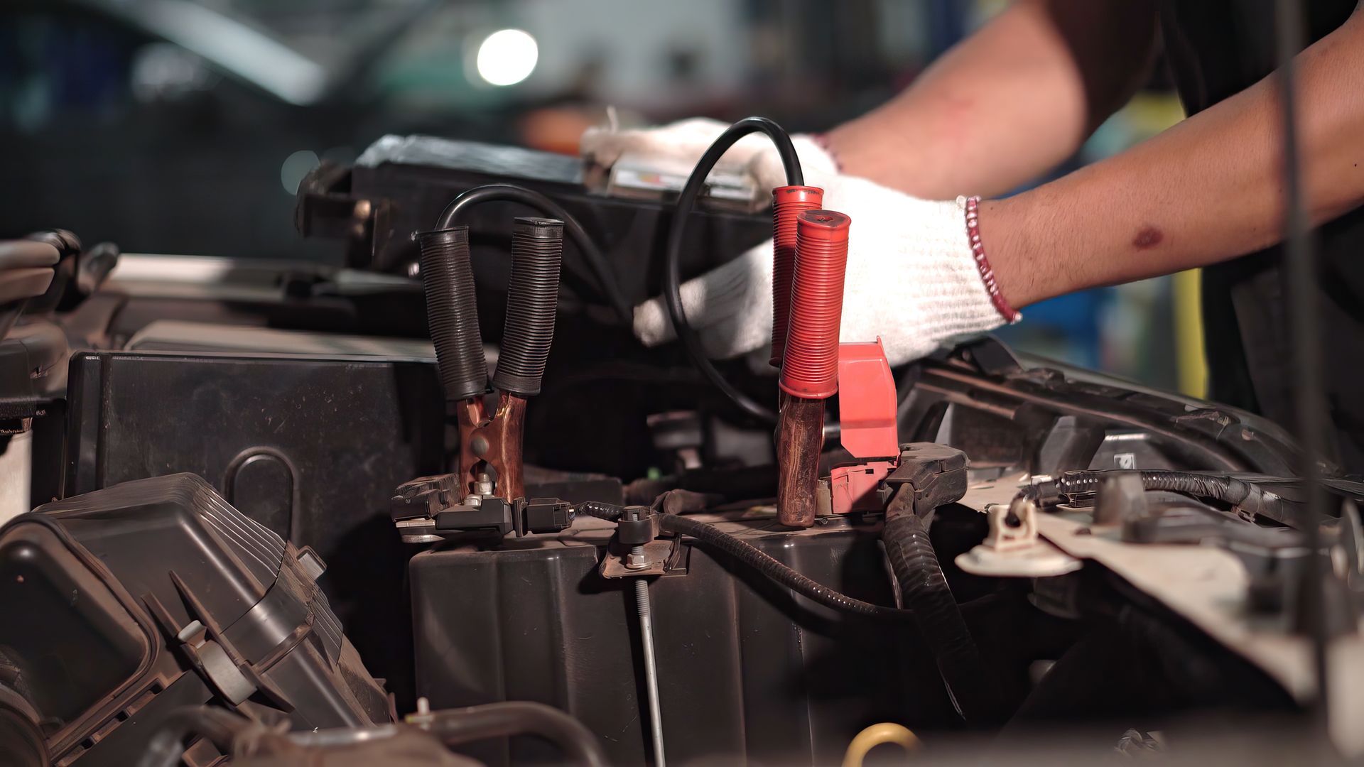 Hands in gloves connecting jumper cables to a car battery in a dimly lit setting. Hands in gloves connecting jumper cables to a car battery in a dimly lit setting.