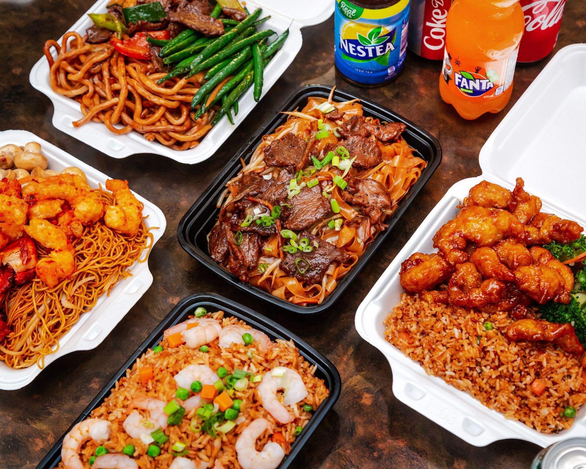 Assorted Japanese dishes in black bowls on a wooden table, including sushi, grilled meat, and tempura vegetables.