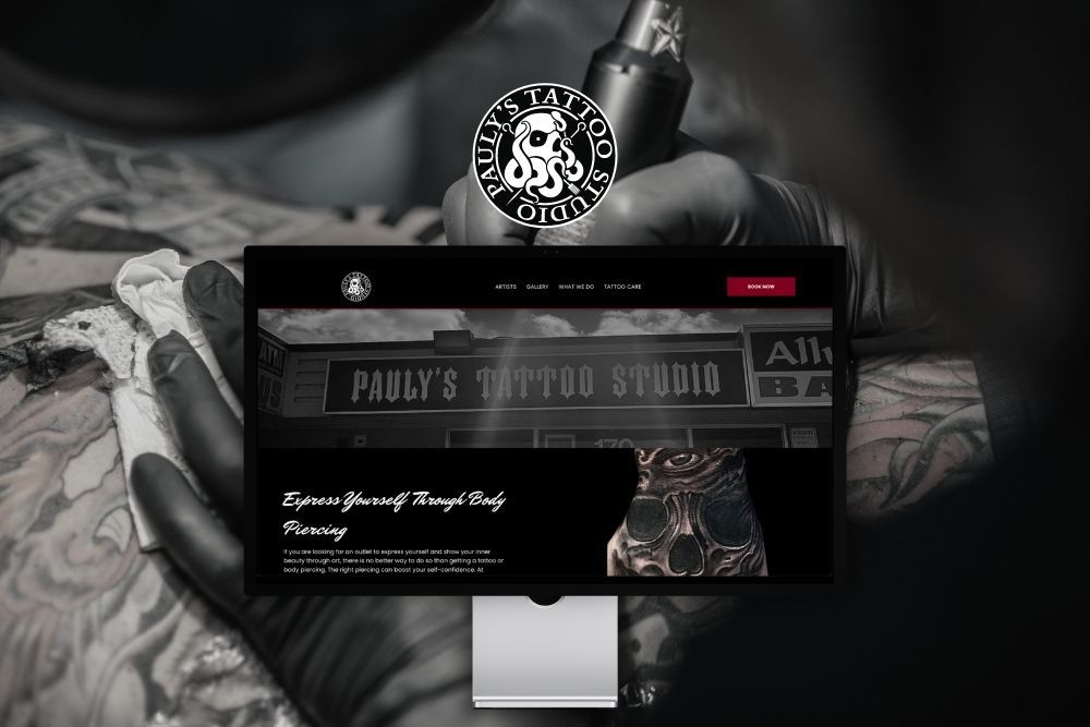 Tattooed hands using a tattoo machine over a client, with a black shop sign reading “Paul’s Tattoo Studio.”