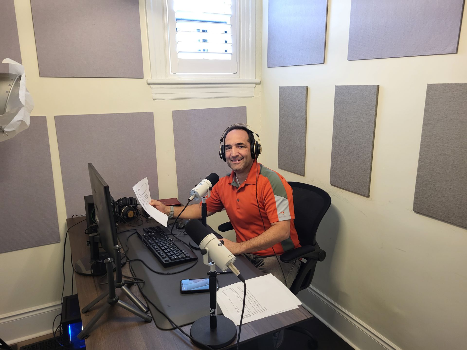 A man wearing headphones is sitting at a desk in front of a microphone.