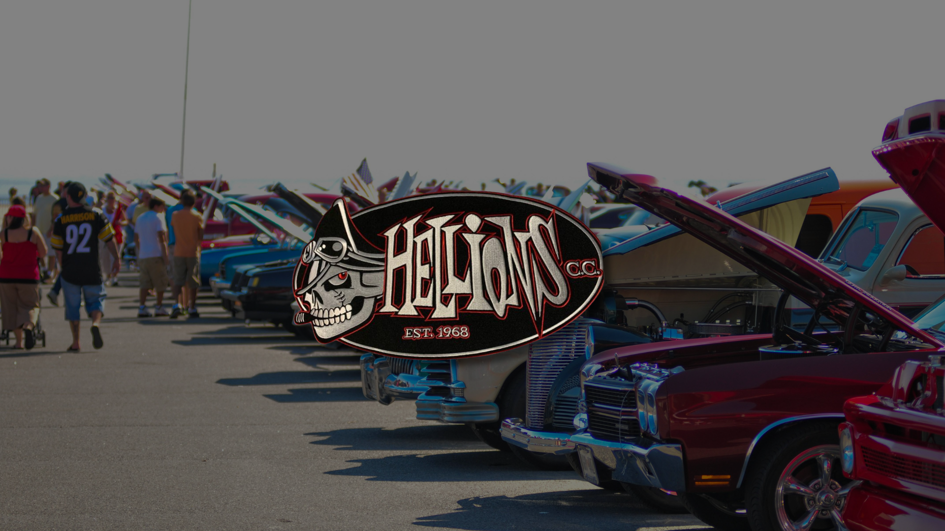 Classic cars lined up on a beach, with a red hot rod in the foreground and a