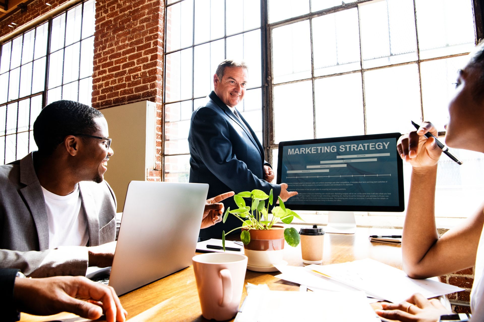 A group of people are sitting at a table in front of a computer discussing a new digital marketing strategy
