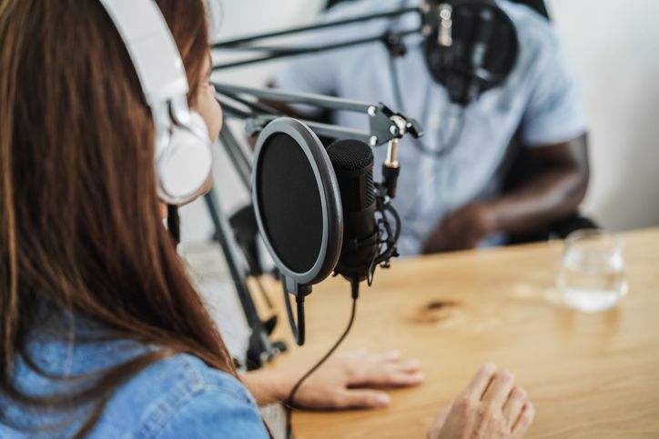 A woman wearing headphones is sitting at a table in front of a microphone.