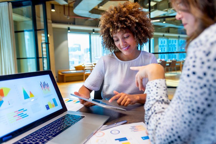 Two women are sitting at a table looking at a laptop computer.