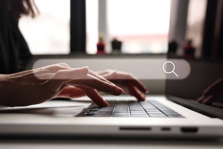 A woman is typing on a laptop computer with a magnifying glass.