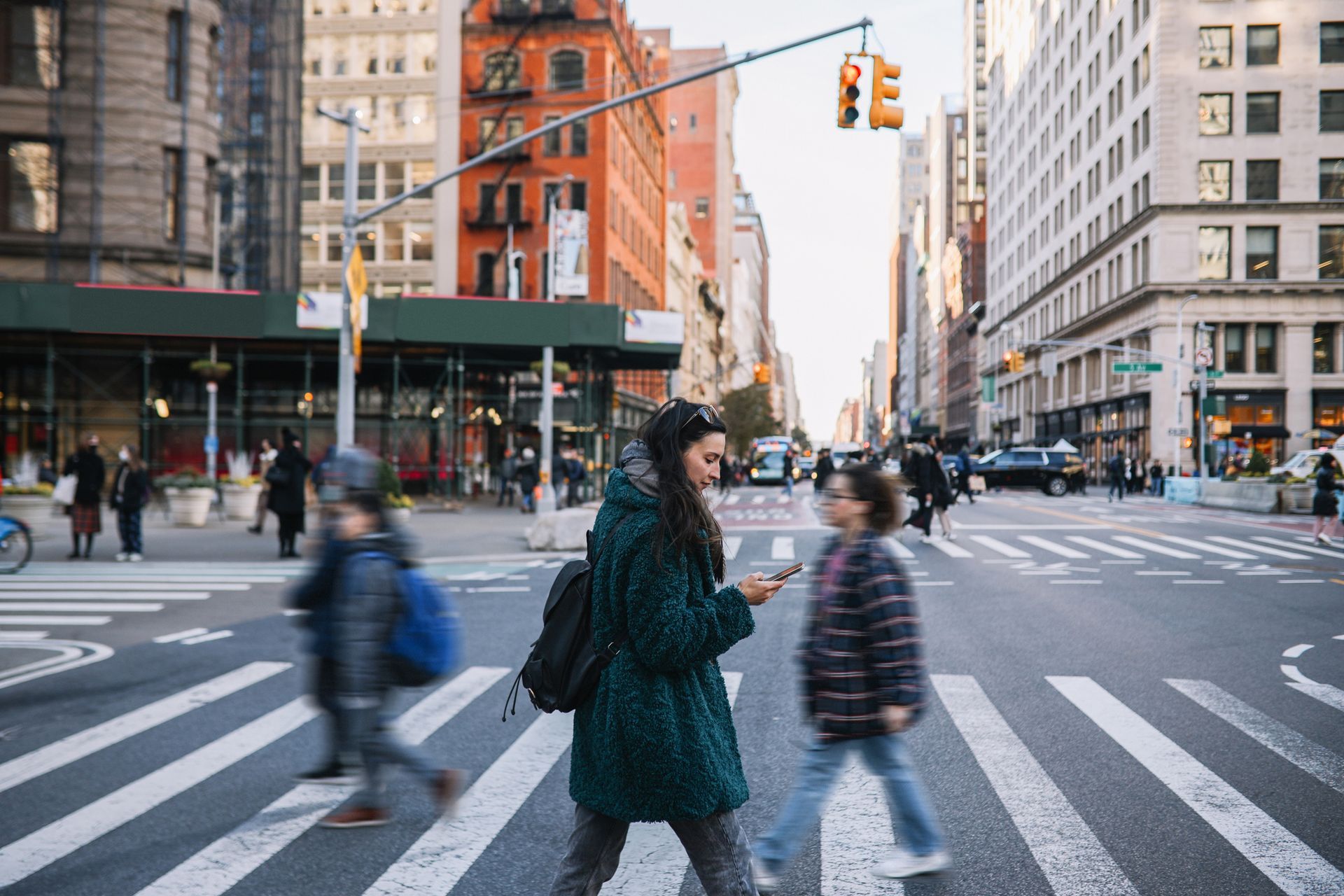 A woman is walking across a busy city street while looking at her phone.