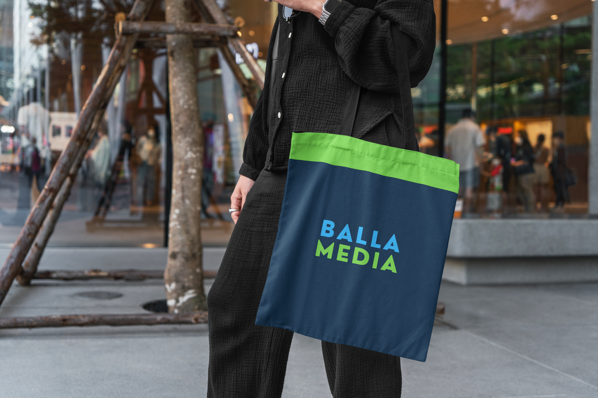 Person carrying a navy tote bag with green trim and “BALLA MEDIA” text on a city street