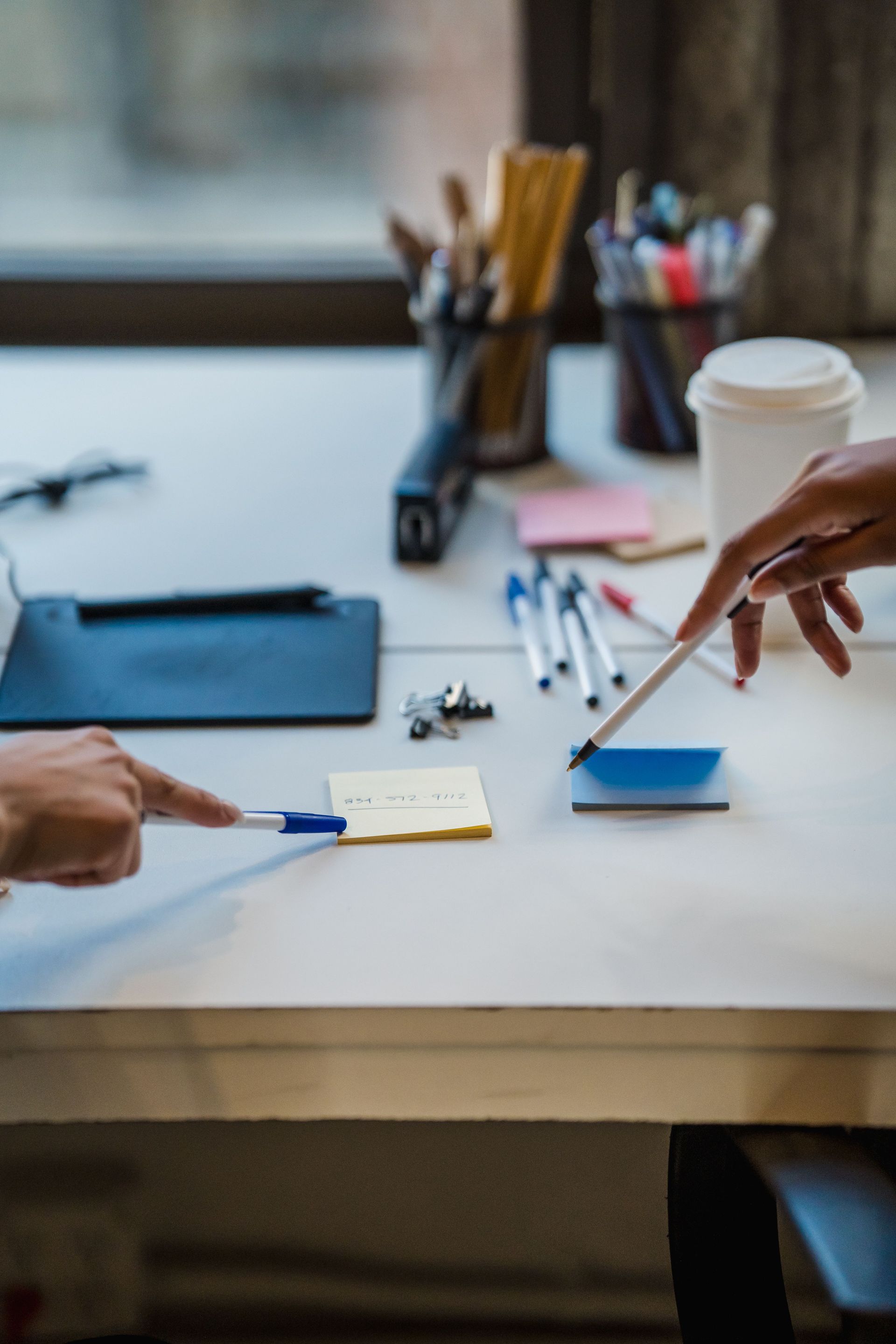 Hands reaching across a desk to exchange cards beside a coffee cup and office supplies