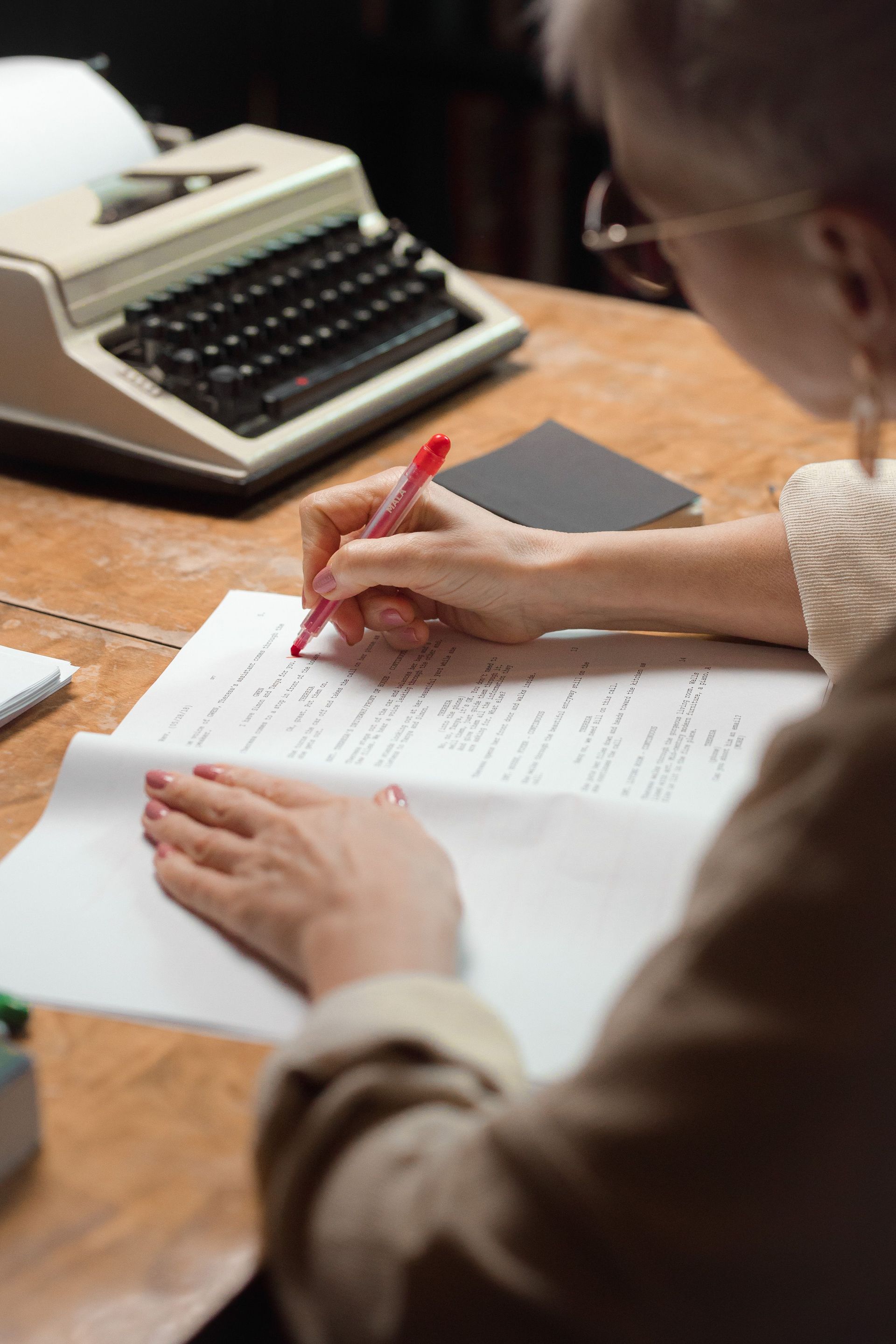 Person writing at a wooden desk beside a vintage typewriter, representing Jo Elizabeth Pinto as an author