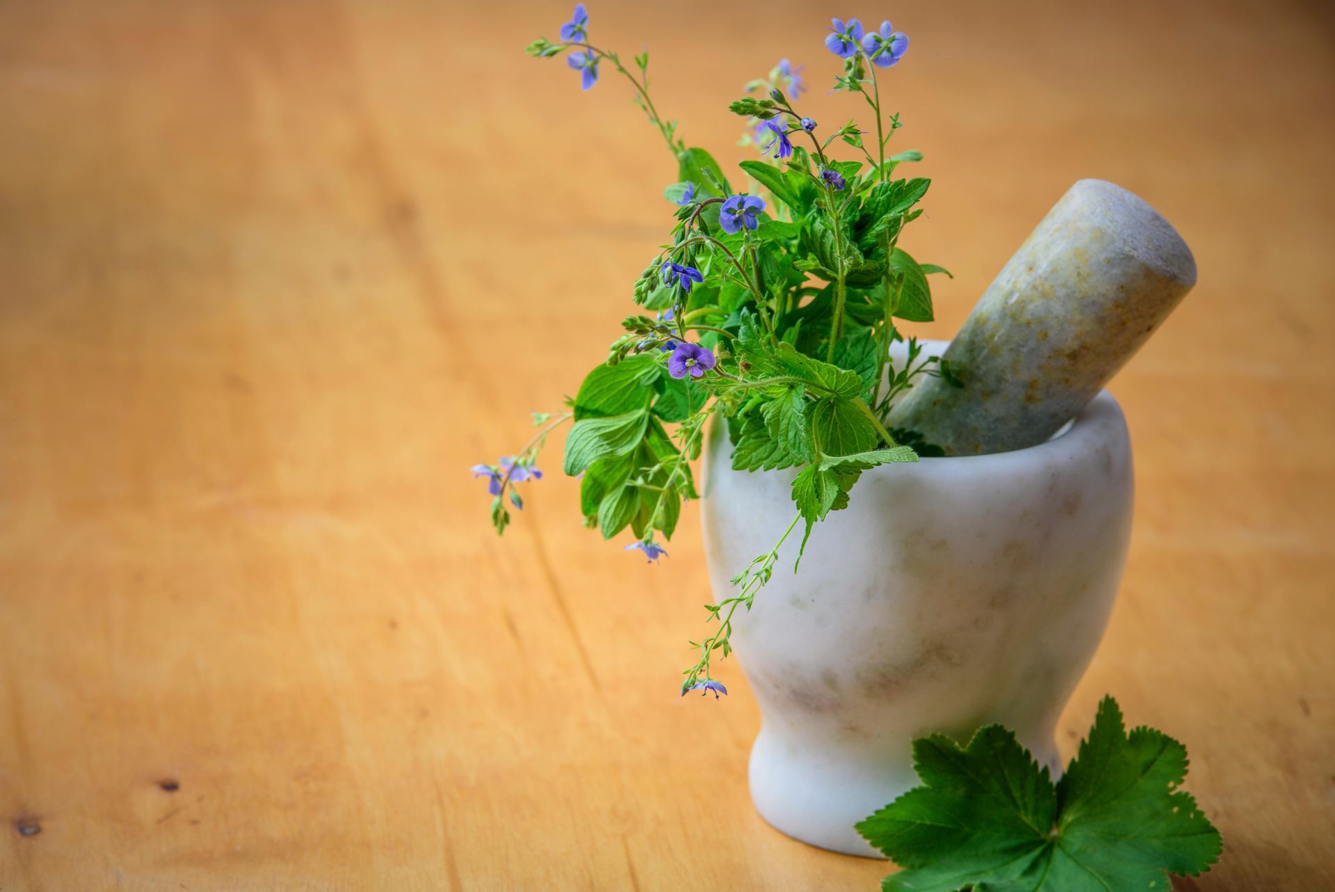 A mortar and pestle with flowers in it on a wooden table.