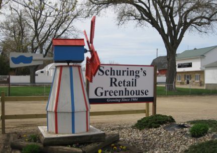 A sign for schuring 's retail greenhouse with a windmill in the background
