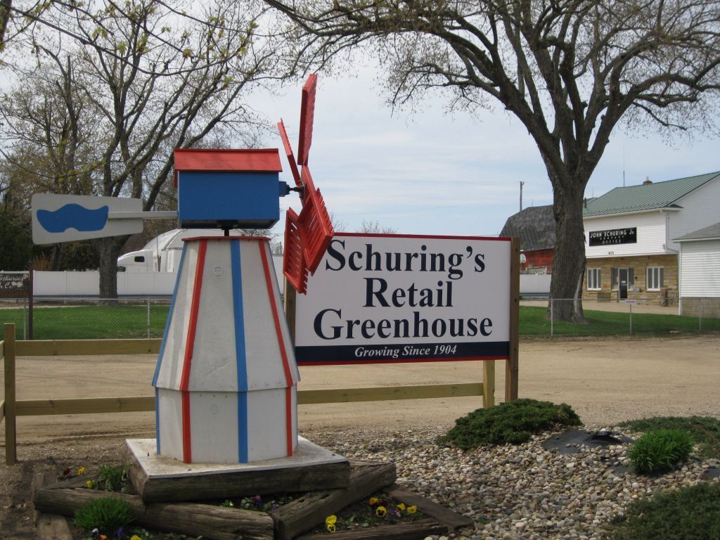 A sign for schuring 's retail greenhouse with a windmill in the background