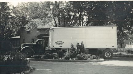 A black and white photo of a moving truck parked in front of a house.