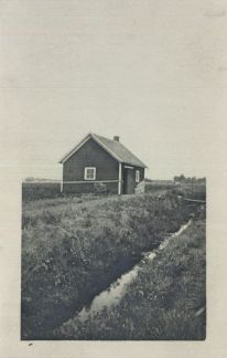 A black and white photo of a small red house in the middle of a field.