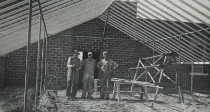 A group of men are standing in front of a brick building under construction.