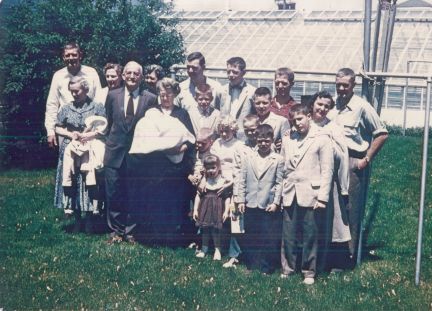 A large family posing for a picture in front of a greenhouse