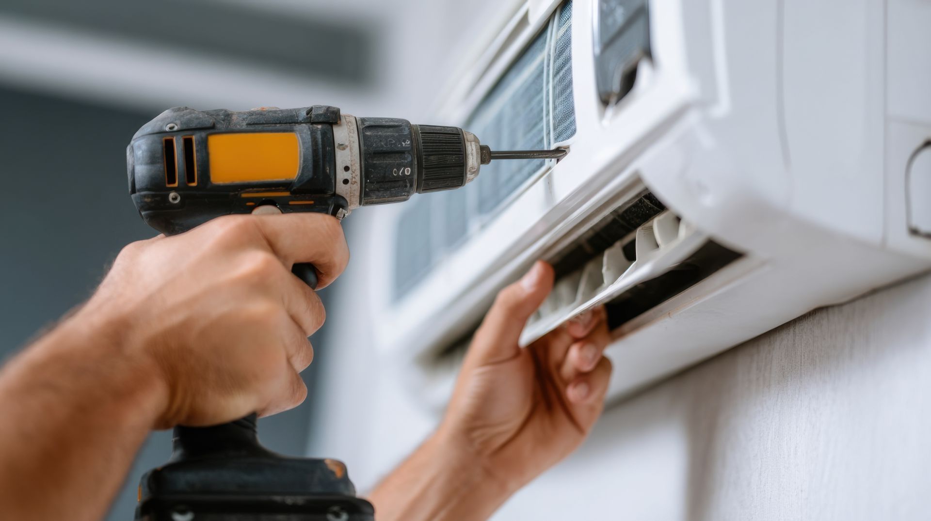 Une personne utilise une perceuse pour installer ou réparer un climatiseur blanc sur un mur blanc.