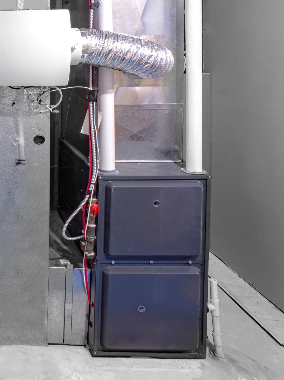 Unité de chauffage avec deux portes d'accès gris foncé ; conduits argentés, tuyaux blancs, contre un mur gris.