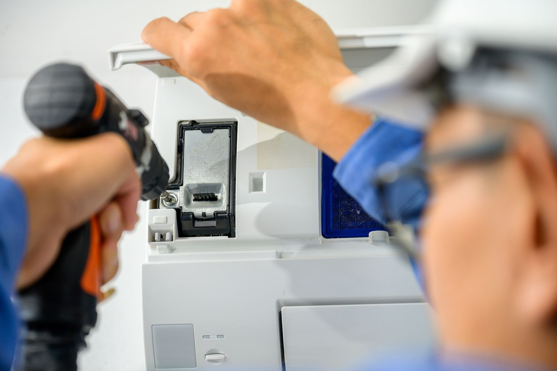 Mains d'une personne utilisant une perceuse électrique et des outils pour réparer un panneau électrique blanc.