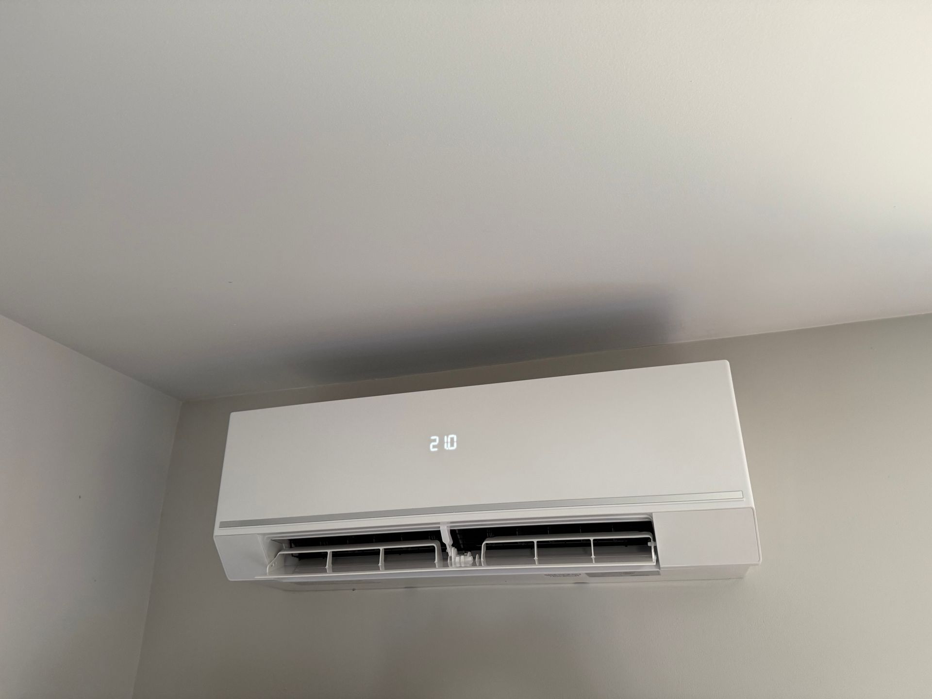 Climatiseur blanc monté sur un mur beige, affichant la température.