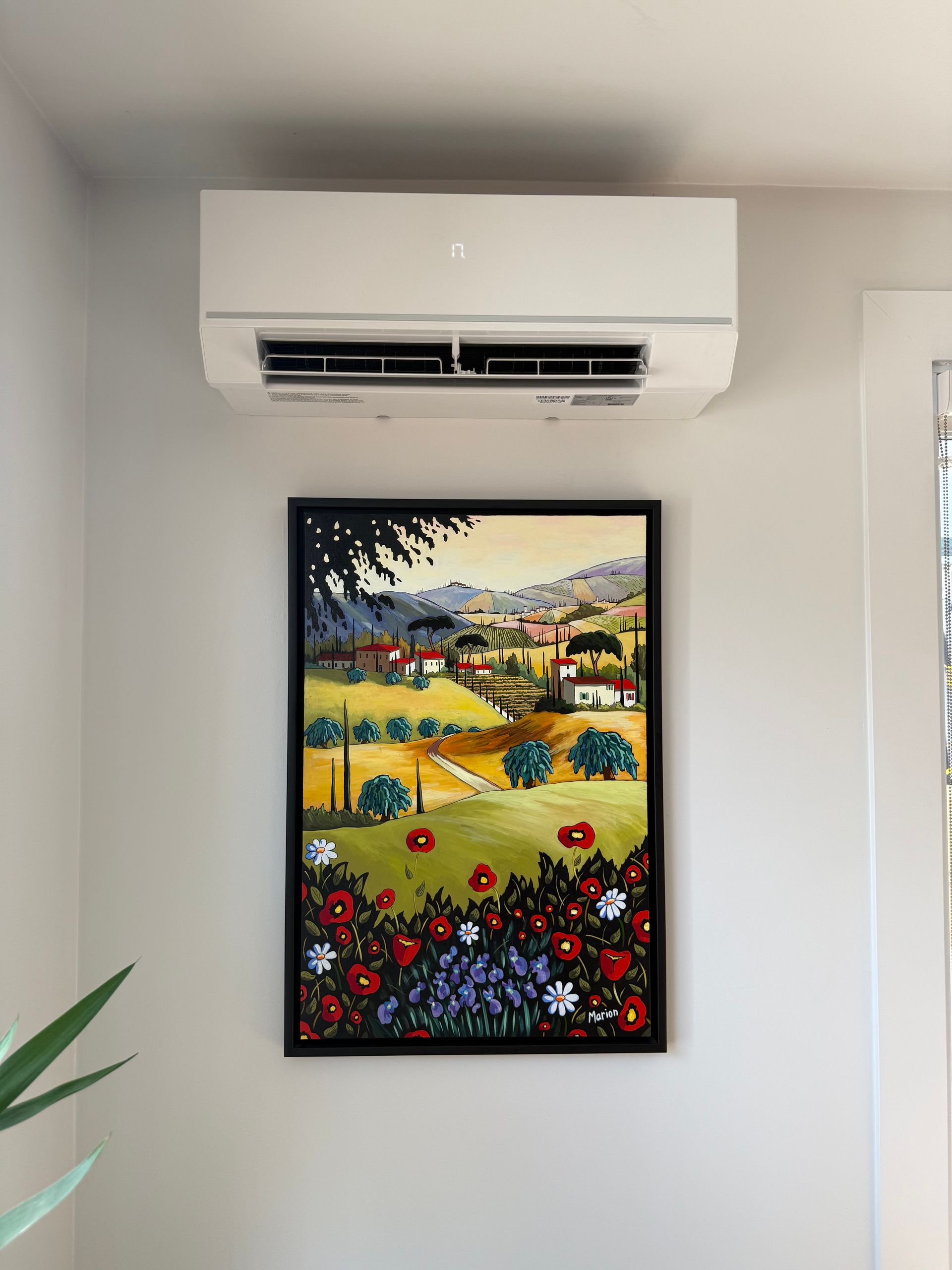 Climatiseur au-dessus d'un tableau encadré d'un paysage coloré avec des fleurs.